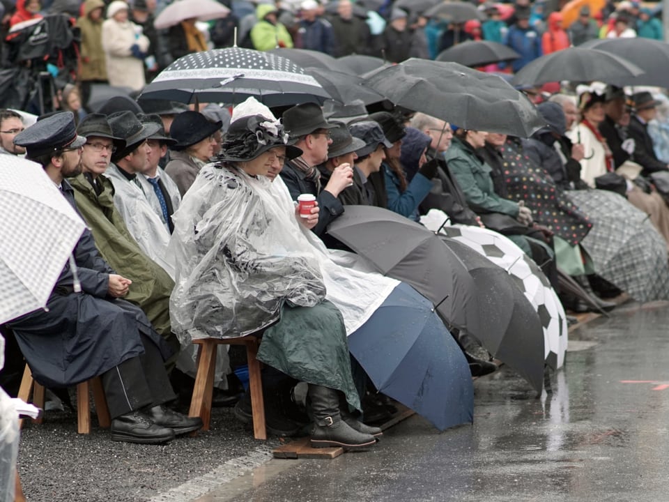 Personen unter Regenschirmen auf einer Bank sitzend