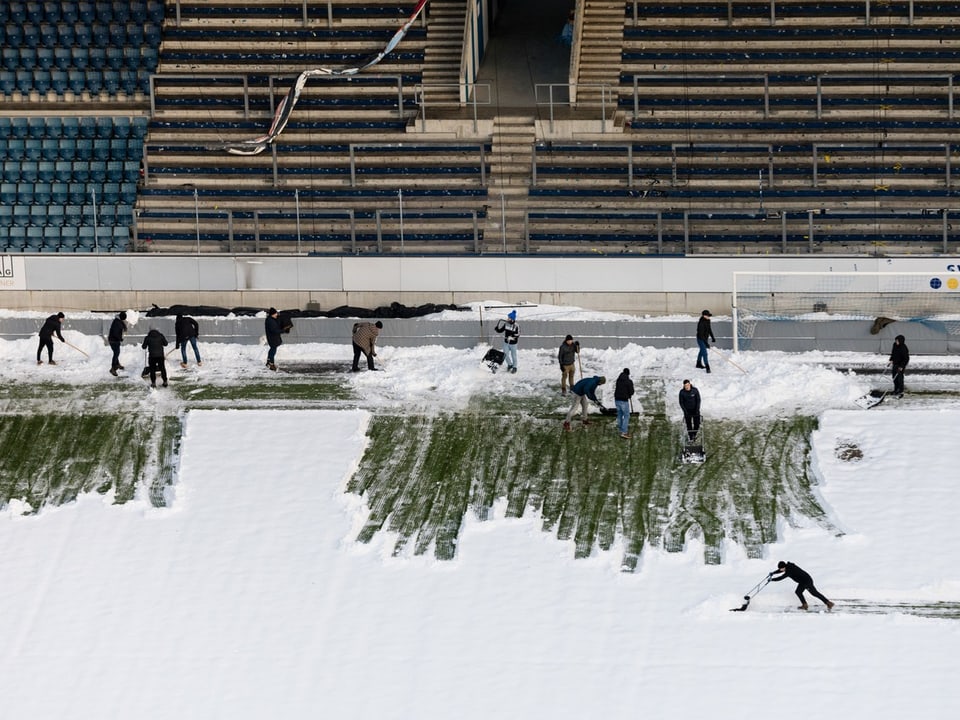 Arbeiter räumen Schnee von einem Fussballfeld im Stadion.