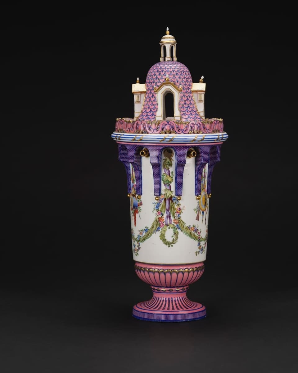 Vase in weiss, rosarot und violett. Deckel in Form eines rosa Turmes, verschnörkelt.