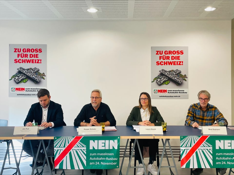 Vier Personen sitzen an einem Tisch mit 'Nein zum Autobahn-Ausbau' Plakaten.