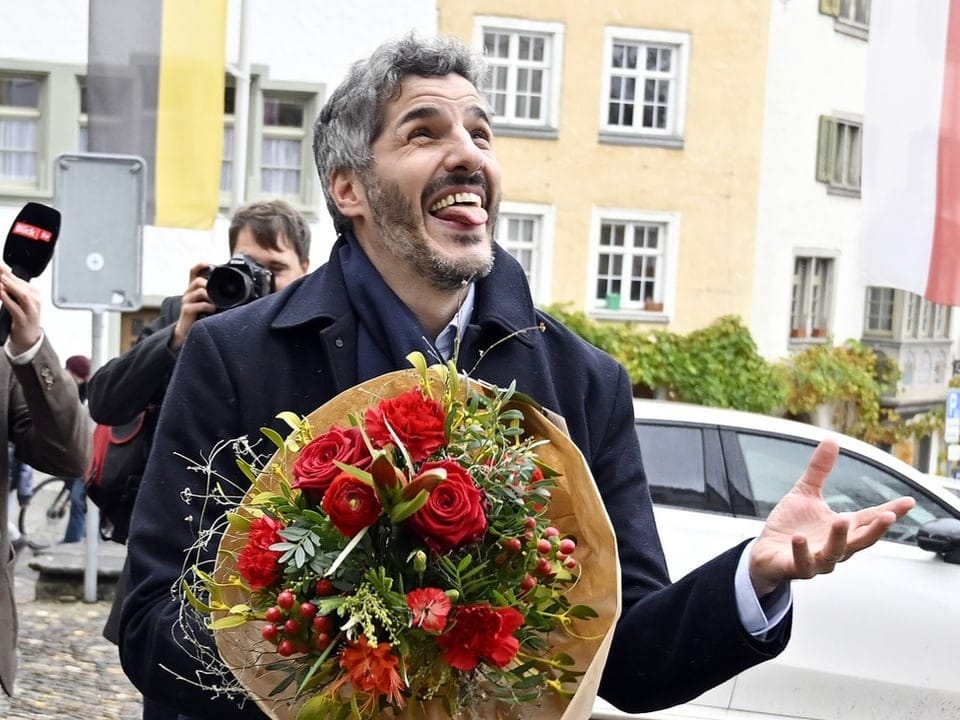 Simon Stocker hält nach seiner Wahl einen Blumenstrauss in der Hand und jubelt.
