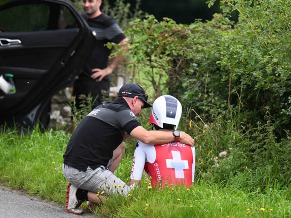 Betreuer tröstet einen Radfahrer mit Schweiz-Trikot am Strassenrand.