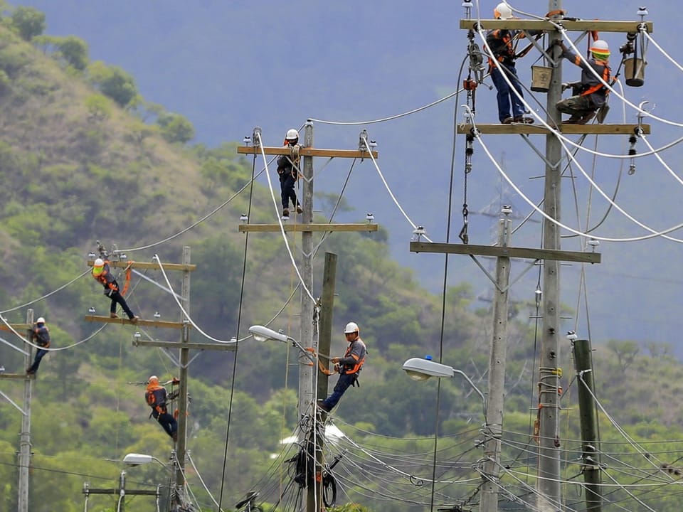 Arbeiter klettern auf Strommasten und installieren neue Leitungen.
