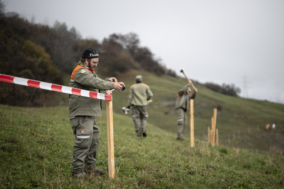 Personen errichten Absperrung im hügeligen Gelände.