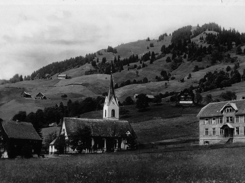 Historisches Foto einer Kirche und Häusern in einer hügeligen Landschaft.