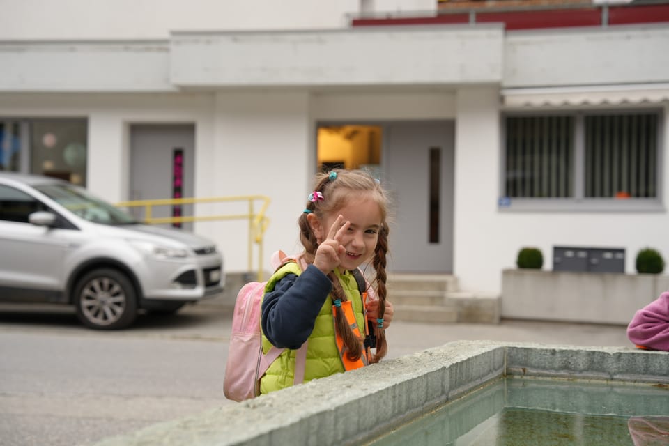 Mädchen zeigt Friedenszeichen neben einem Brunnen.