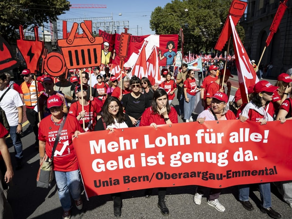 Menschenmarsch mit Bannern, der höhere Löhne fordert.