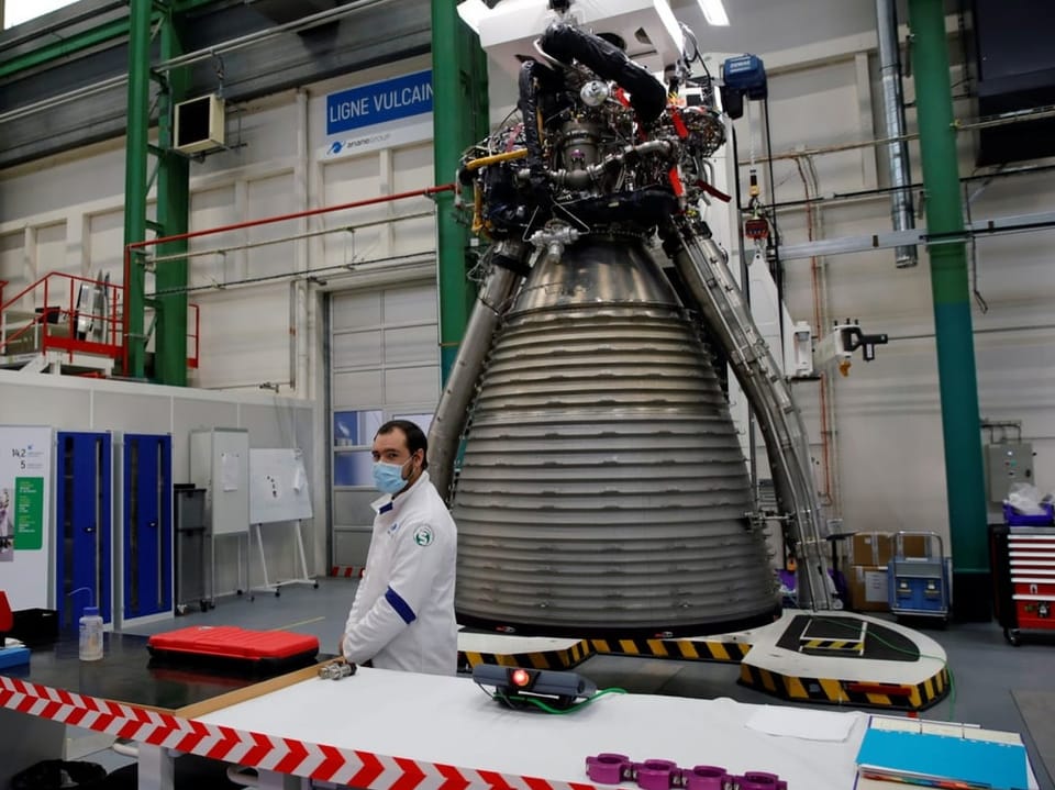 Techniker mit Mundschutz steht vor einer grossen Raketenantriebseinheit in einer Werkshalle.