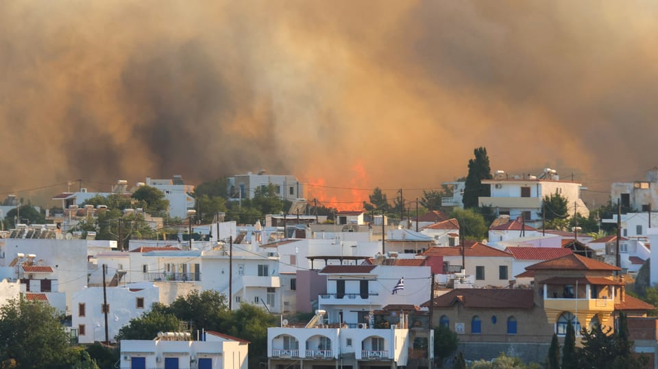 Flammen und Rauch steigen hinter einem Dorf auf.