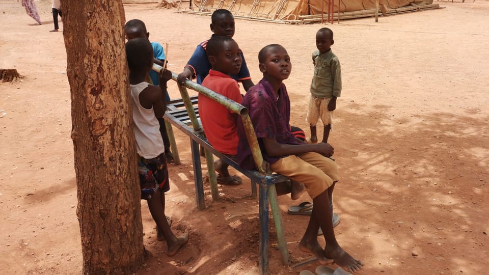 Kinder sitzen im Kriegsgebiet im Sudan auf einer Bank vor einem Zelt