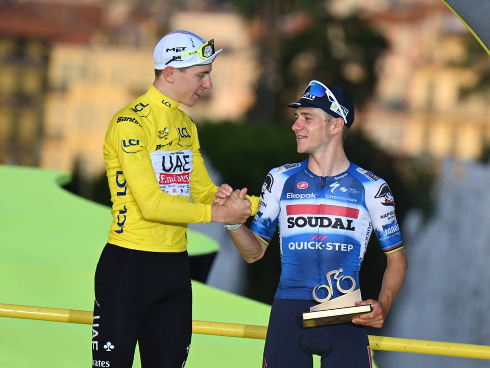 Zwei Radfahrer im gelben bzw. blauen Trikot gratulieren sich auf dem Podium.