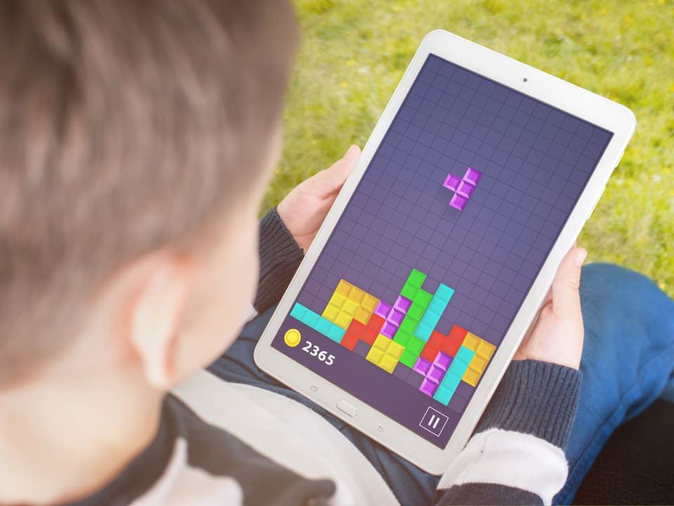Ein Kind spielt auf dem Tablett eine bunte Variante von Tetris.