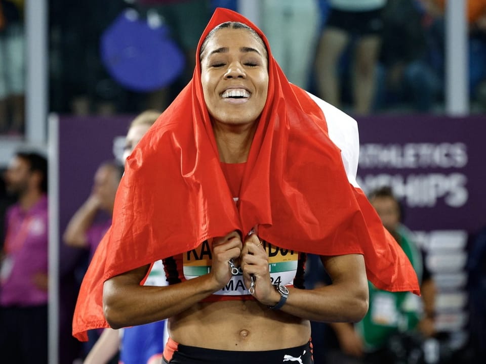 Eine Athletin mit einer Nationalflagge über dem Kopf, feiert.