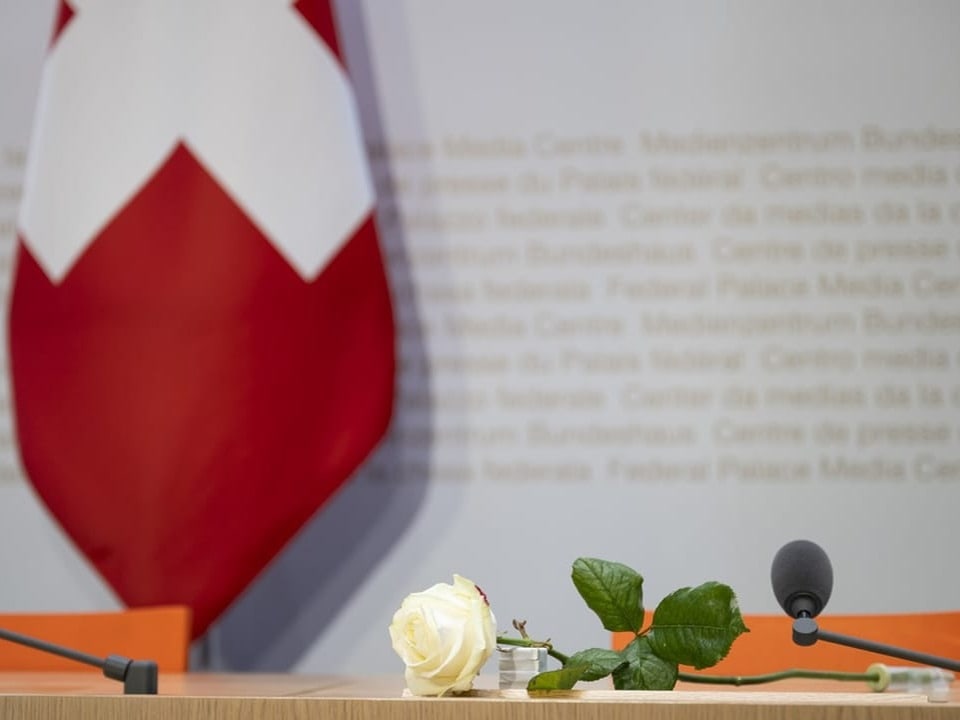 Weisse Rose auf Tisch vor Schweizer Fahne und Mikrofon.