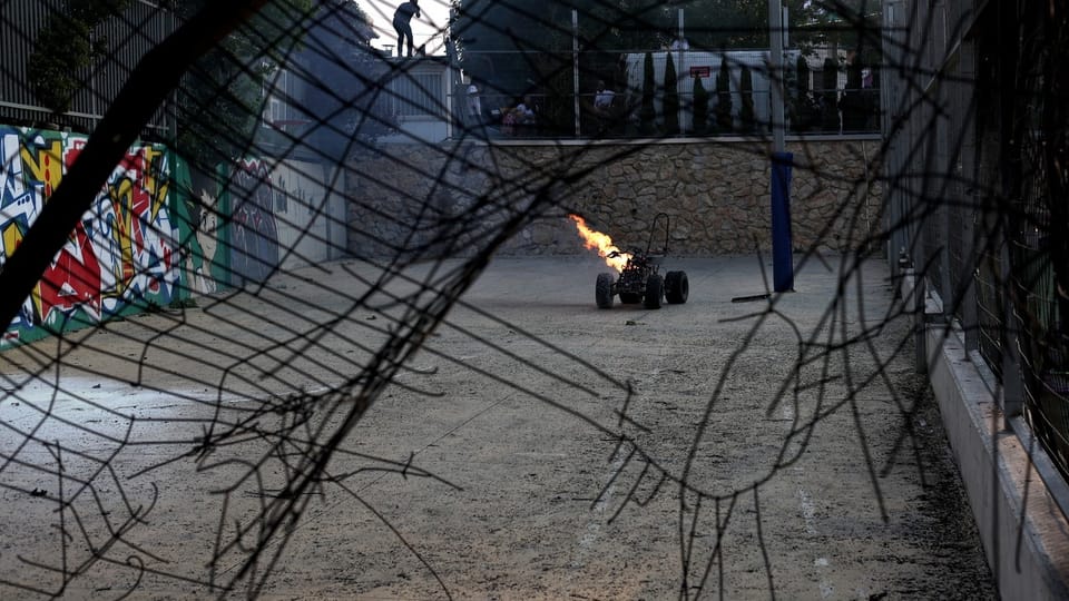 Ferngesteuertes Auto mit Flamme in kaputtem Zaunbereich.