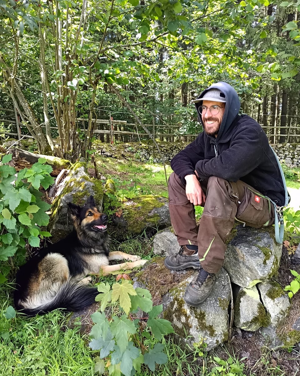 Mann sitzt mit Hund auf Steinen im Wald.