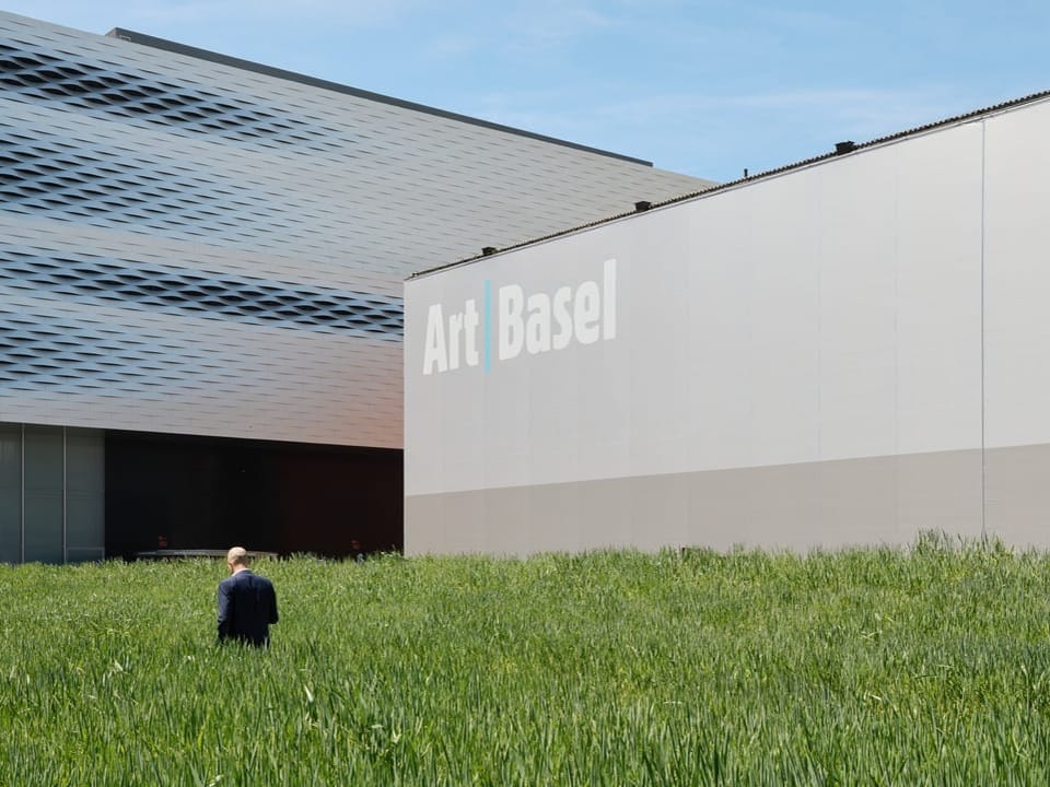 Person auf einem grasbewachsenen Feld vor dem Gebäude von Art Basel.