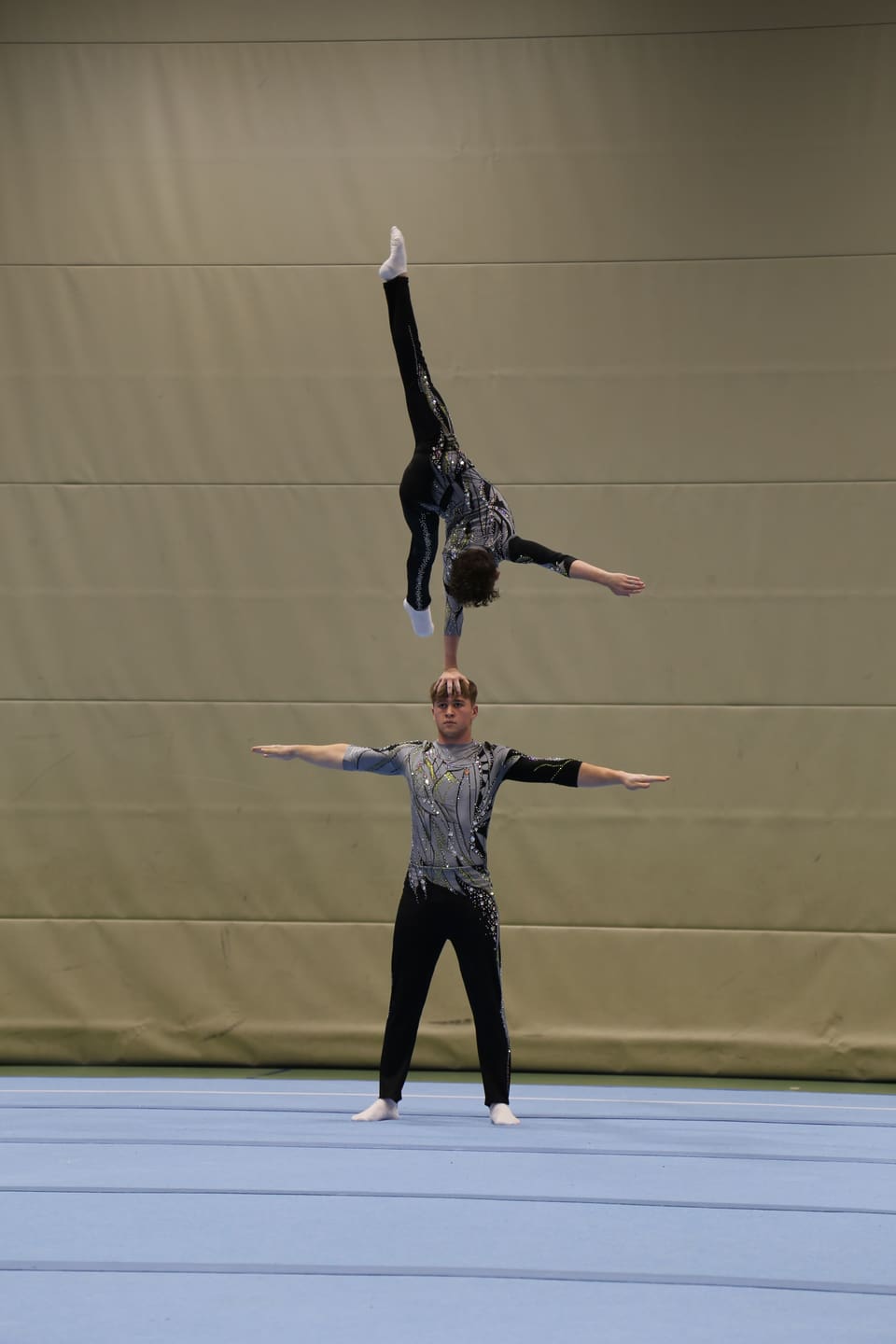 Zwei Turner in Akrobatikpose auf blauer Matte.