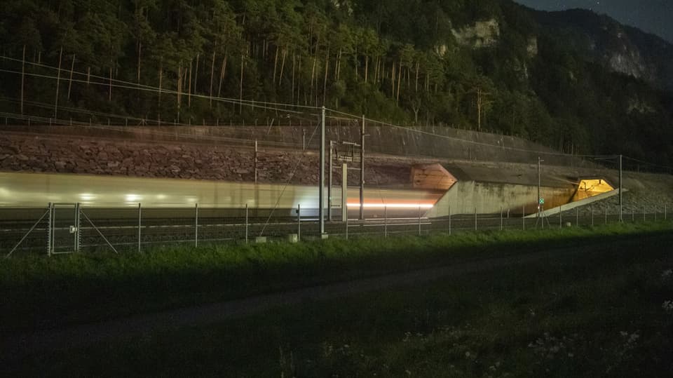 Blick auf Tunnelportal bei Nacht mit Lichtspur von vorbeifahrendem Zug