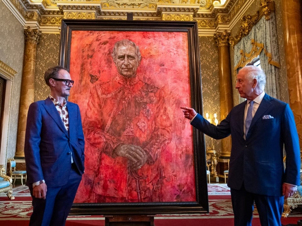 Zwei Männer stehen neben einem Porträt in einem prunkvollen Raum.