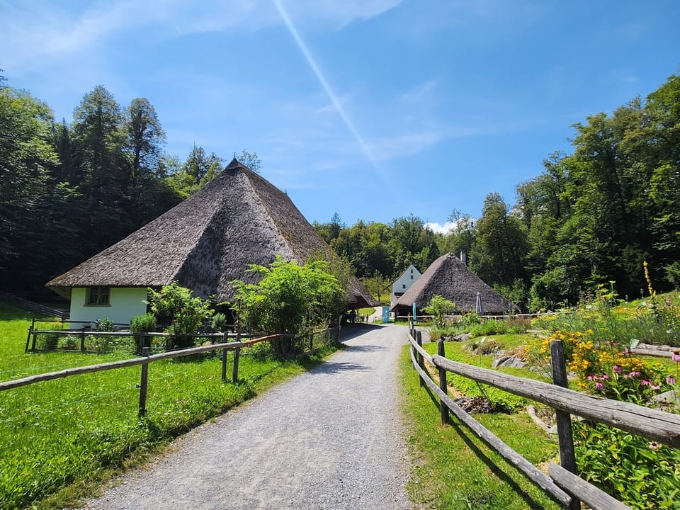 Schotterweg führt zu strohgedeckten Häusern in ländlicher Umgebung.