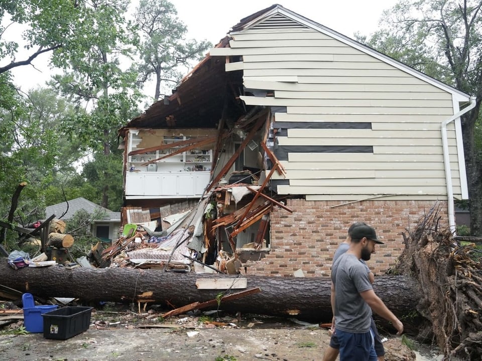 Haus mit zerstörter Fassade durch umgefallenen Baum, Mann im Vordergrund.