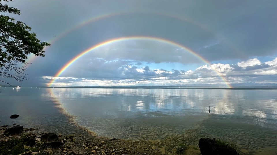 Doppelter Regenbogen über einem ruhigen See.