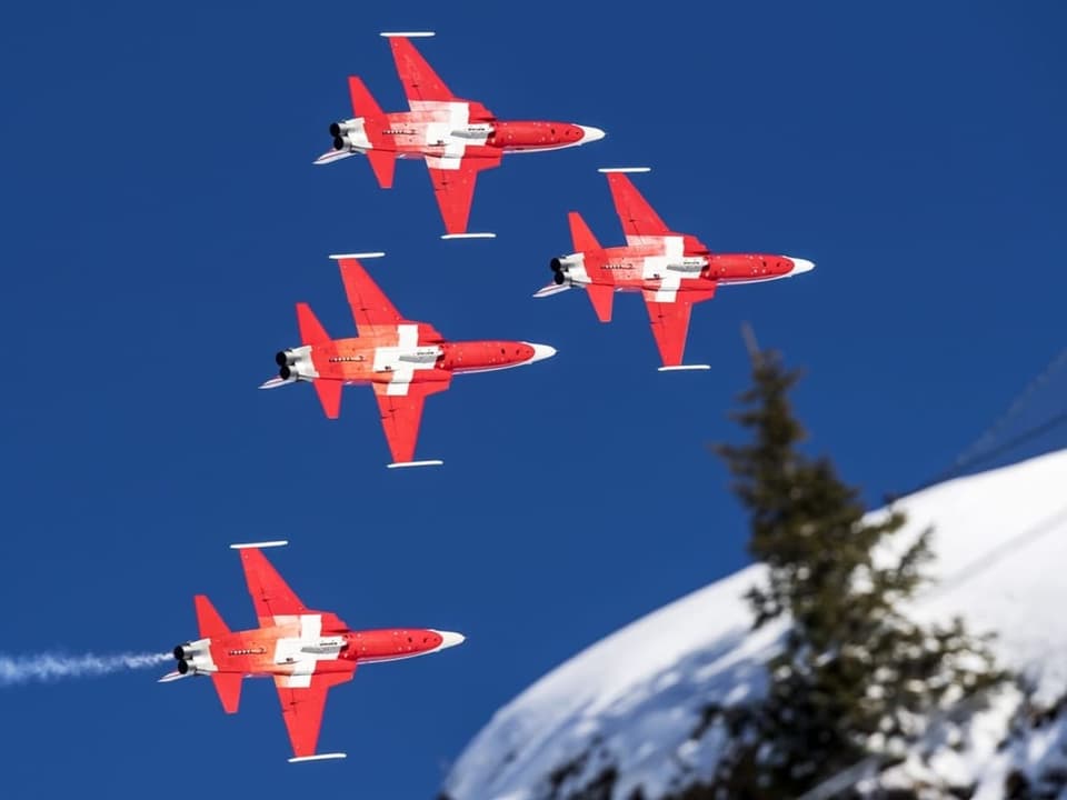 Vier rotweisse Jets fliegen in einer Formation über einen Schneehügel. 