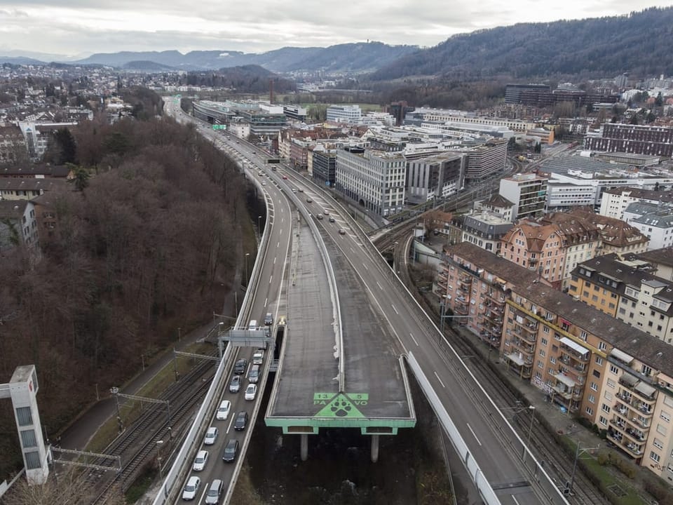 Luftaufnahme einer Autobahn, die durch eine städtische Gegend führt, mit Wohngebäuden und Hügeln im Hintergrund.