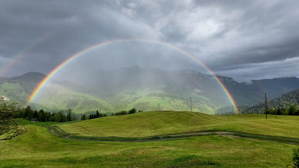 Doppelter Regenbogen über grünen Hügeln und Bergen.