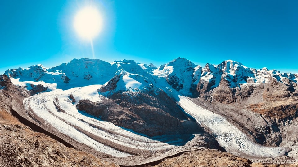 Panorama des Gletschers mit schneebedeckten Bergen und Sonne.