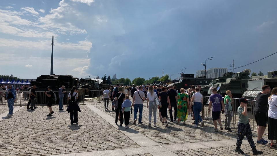 People stroll through a square where tanks are on display