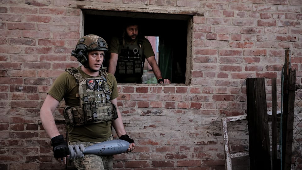 Gewehr und Uniform tragende Soldaten bei einer Ziegelmauer.