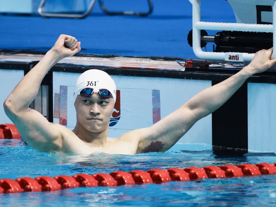 Schwimmer hebt Arm im Pool nach Wettkampf.