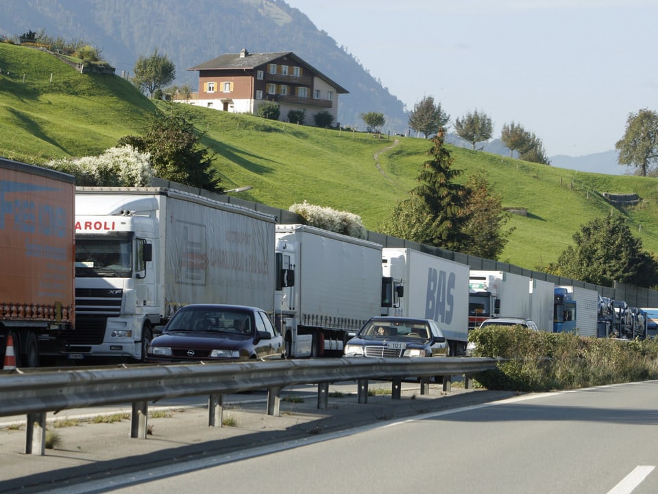 LKW-Stau auf Autobahn mit ländlicher Kulisse und Haus im Hintergrund.