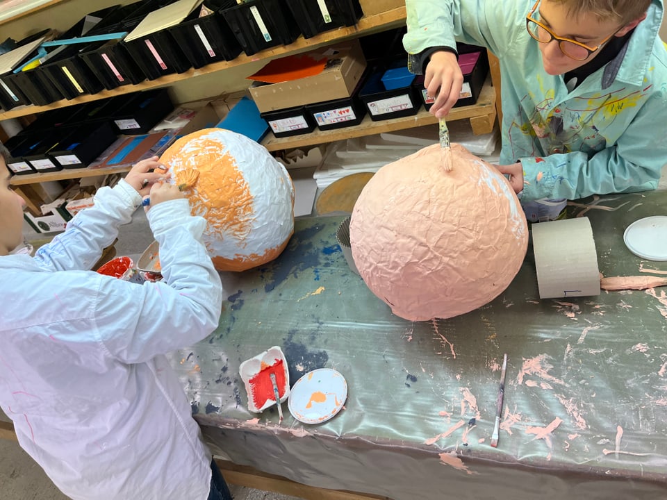 Kinder malen die Masken von Martin Candinas an auf einem Tisch.