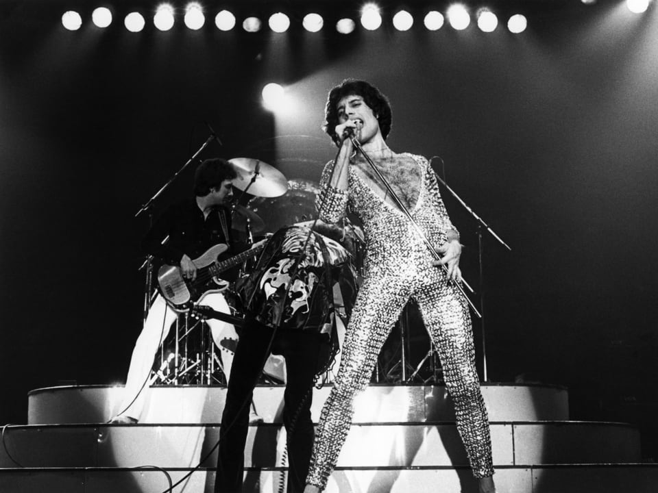 Freddie Mercury performt auf der Bühne im engen Glitzerkleid.
