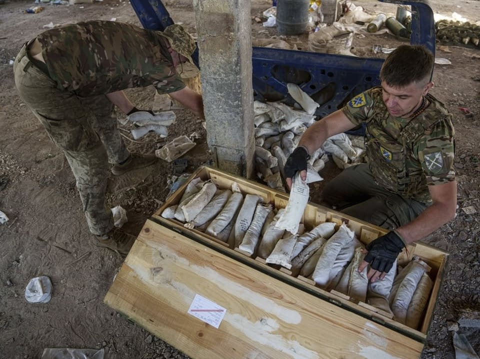 Zwei Soldaten packen Munition in eine Kiste.