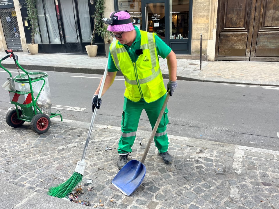 Lucovic, der Strassenreiniger, in grün-gelber Uniform mit Besen und Schaufel.