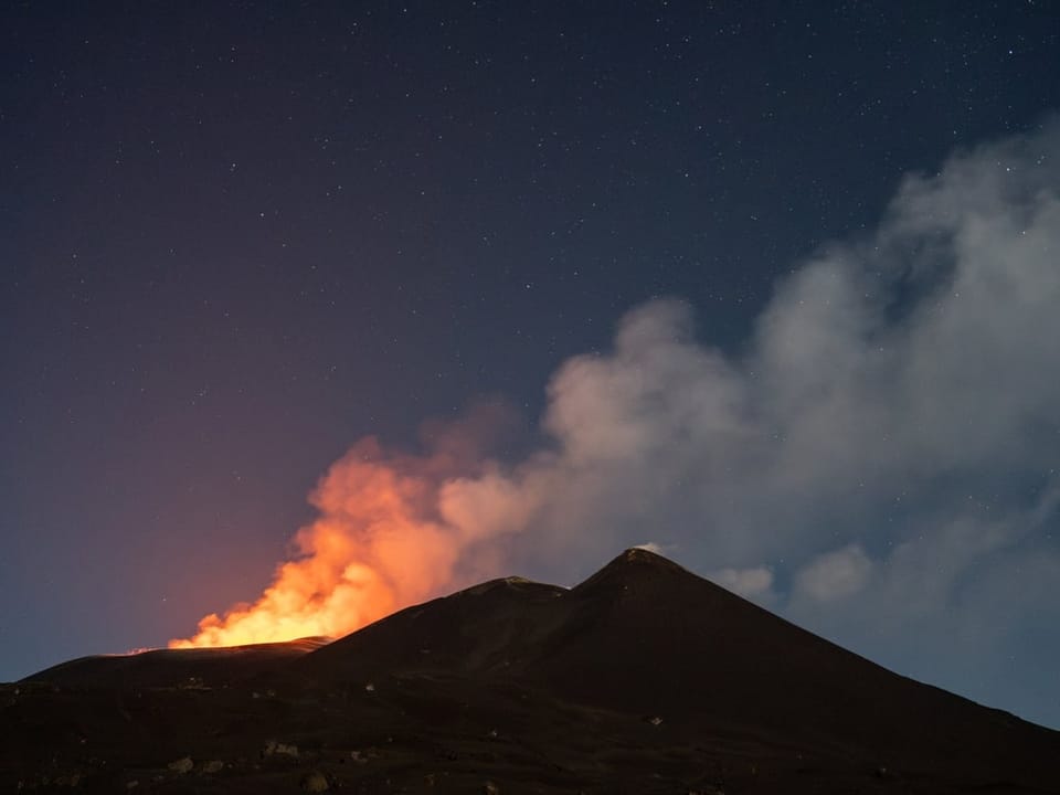 Vulkan in der Nacht mit glühender Lava und Sternenhimmel.
