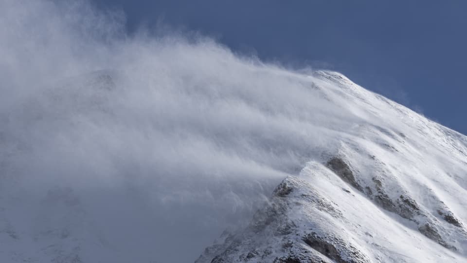 Wind weht Schnee über einen schneebedeckten Berg.