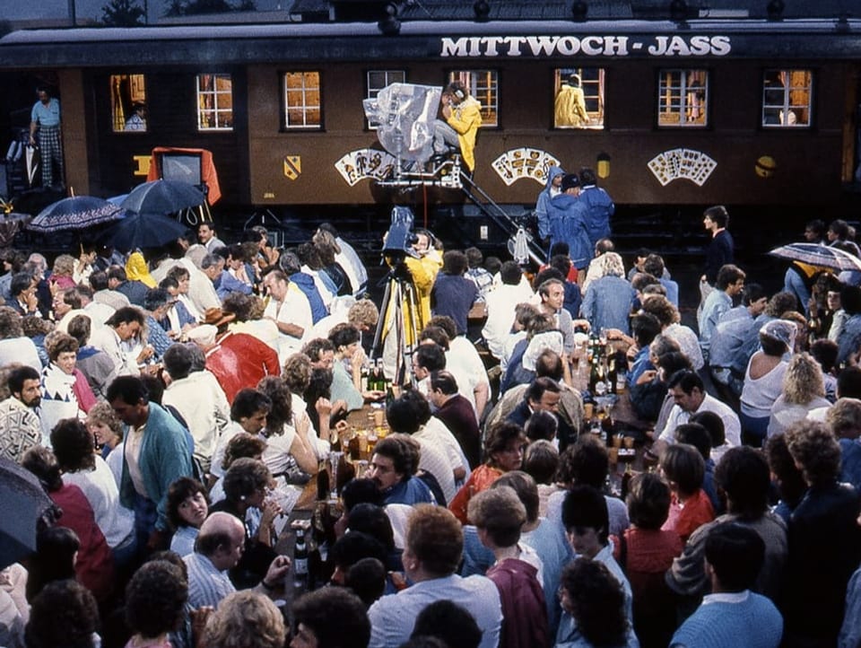 Eisenbahnwagen, davor Zuschauerinnen und Zuschauer auf Festbänken