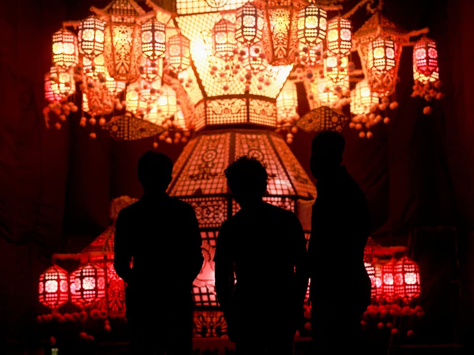 Silhouette of three people in front of red lanterns.