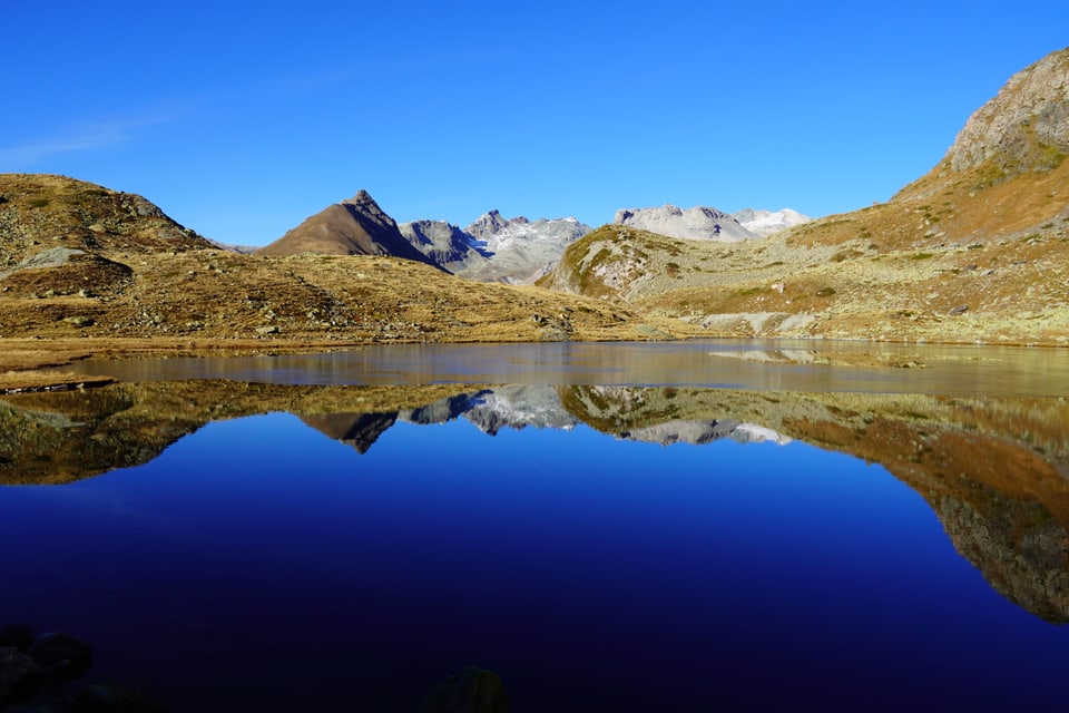 Bergsee mit Bergspiegelung unter klarem Himmel.