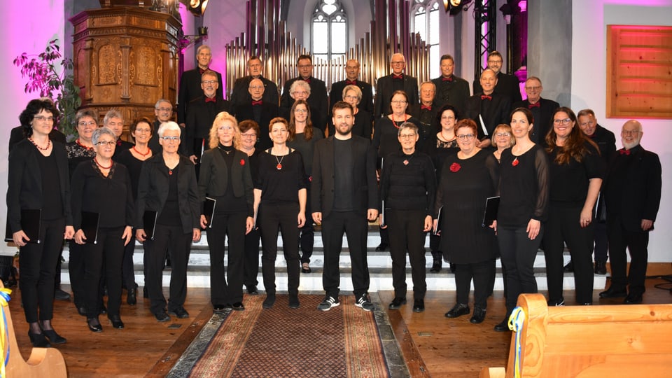 Chor mischedau Suraua, der gemischte Chor steht in einer Kirche, gekleidet ganz in schwarz.