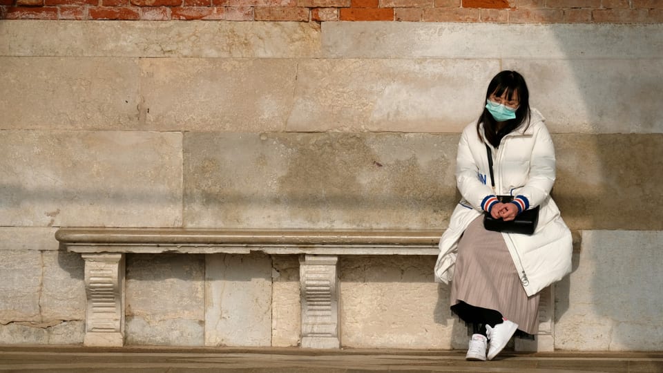 Chinesin mit Gesichtsmaske sitzt einsam auf einer Steinbank.