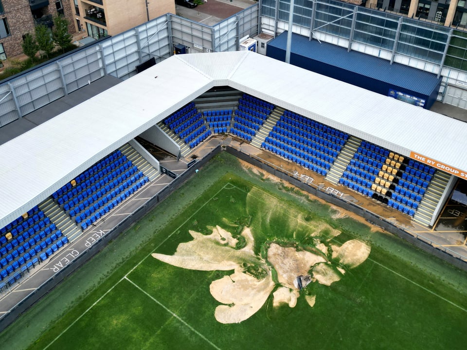 Luftaufnahme eines Fussballstadions mit beschädigtem Spielfeld.