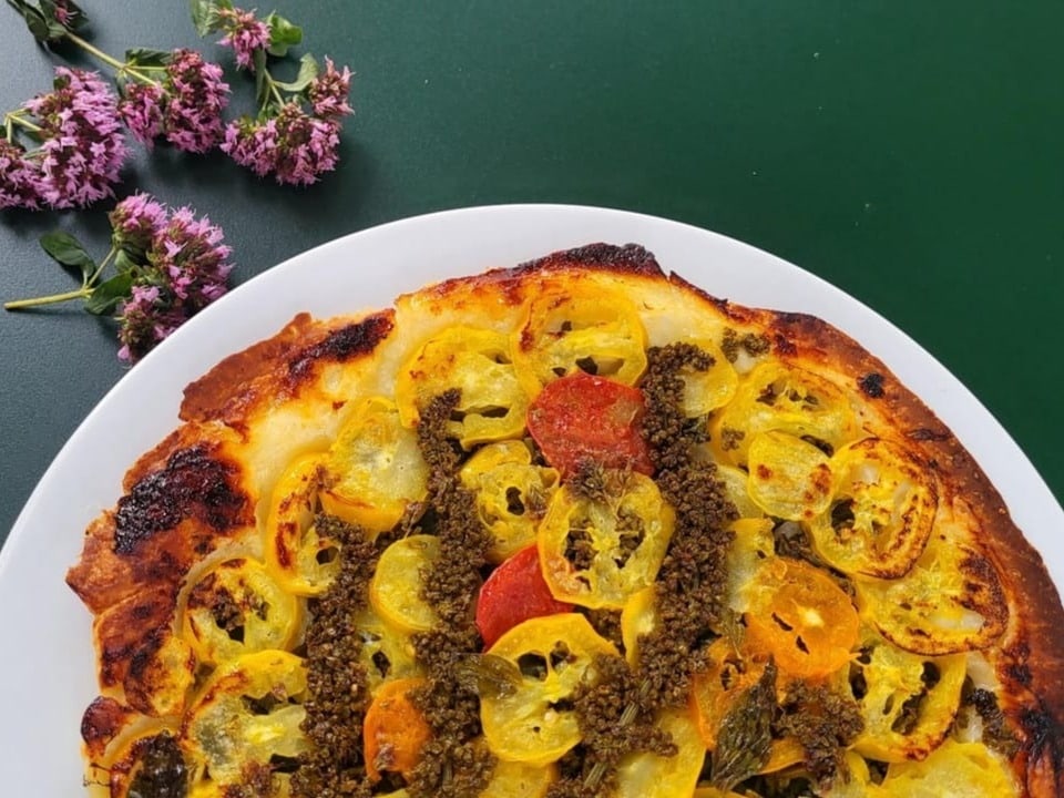 Salzige Tarte Tatin mit Tomaten und Guter Heinrich auf weissem Teller auf dunkelgrünem Tisch