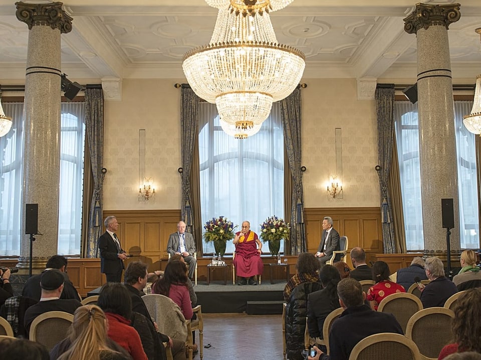 Dalai Lama sitzt auf einem Stuhl in einem pompösen Raum