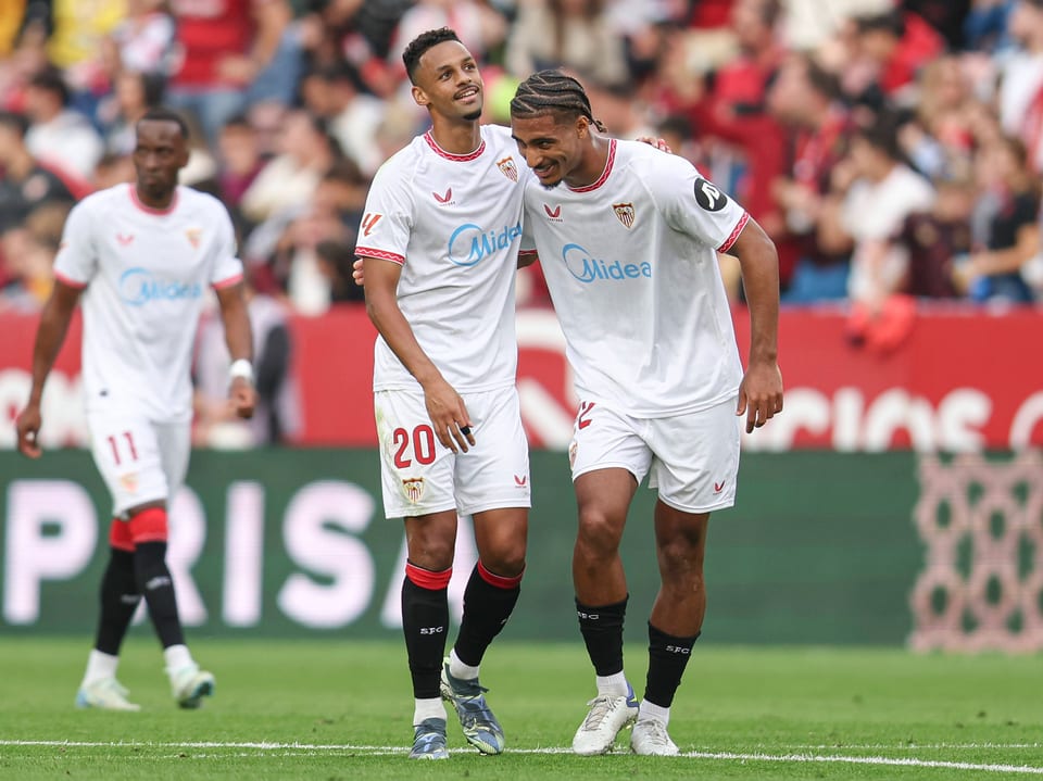 Zwei Fussballspieler von Sevilla auf dem Spielfeld, einer legt einem Arm um den anderen.